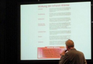 Photo of male speaker facing powerpoint slide with lots of words written on it..